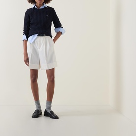 Model wearing Gant Cable Knit Logo Sweater in Dark Blue with white shorts, blue shirt collar, grey socks and black loafers
