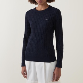 Model wearing Gant Cable Knit Logo Sweater in dark blue with crew neck and cable knit texture, styled with white trousers