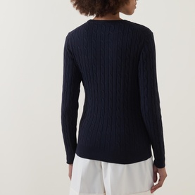 Model wearing Gant Cable Knit Logo Sweater in Dark Blue, showing ribbed cable-knit back detail and long sleeves, styled with white trousers