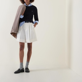Model wearing Gant Cable Knit Logo Sweater in dark blue with crew neck, styled with white shorts and black loafers, carrying a beige jacket