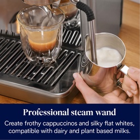 De'Longhi La Specialista Arte Evo in silver, steam wand frothing milk in steel jug alongside a glass of espresso