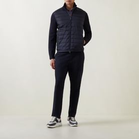Model wearing Moncler Padded Quilted Zip Cardigan in navy with knitted sleeves and high collar, styled with navy trousers and grey trainers