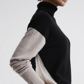 Model wearing Reiss Alexis Colour-Block Sweater in beige, featuring roll-neck and contrast black and oatmeal knit sleeves with ribbed cuffs
