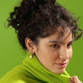 Model with Newbridge Sappho Baroque Pearl Earrings in gold-plated drop design, styled with a lime green turtleneck jumper