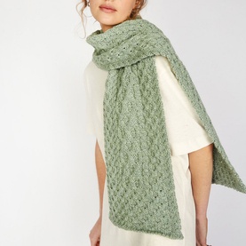 Model wearing Irelands Eye Aran Chunky-Knit Scarf in green merino wool with honeycomb and lattice stitch detail, styled over white top