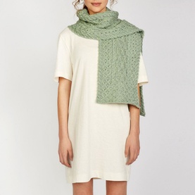 Model wearing Irelands Eye Aran Chunky-Knit Scarf in green, draped over cream mini dress, featuring honeycomb and cable knit detailing
