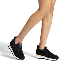 Model wearing Kurt Geiger Lara Embellished Slip-On Trainers in black with crystal embellishment, gold-tone zip detail, and white sole