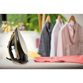 Tefal Ultimate Turbo Pro steam iron in black and gold on ironing board, with hanging garments and folded clothes in background
