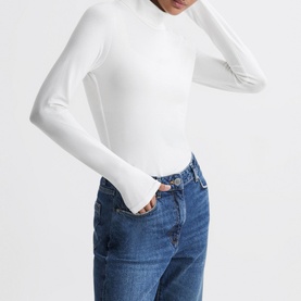Model wearing Reiss Piper Roll Neck Fitted Top in white, long sleeves with cuffed wrists, styled with blue denim jeans