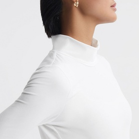 Model wearing Reiss Piper Roll Neck Fitted Top in white, close-up showing rolled neckline and long sleeve detail, with gold earring visible
