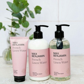 Max Benjamin French Linen Water hand lotion, hand and body lotion, and hand and body wash in pink pump bottles displayed with greenery