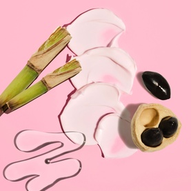 Sol De Janeiro Beija Flor Elasti-Cream body cream shown with pink lotion swatches, bamboo stems and black stones on pink background