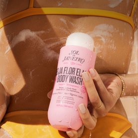 Sol de Janeiro Beija Flor Body Wash pink bottle held by model with gold bracelet, foam visible against skin