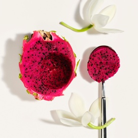 Sol De Janeiro Beija Flor Body Wash ingredient shot featuring halved dragon fruit, white flower petals and a spoon on a light background.