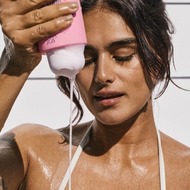 Model pouring Sol De Janeiro Beija Flor Body Wash, pink bottle, onto wet skin, wearing a white bikini top