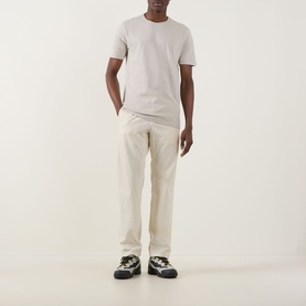 Model wearing Hugo Boss Orange Tales Logo T-Shirt in beige, crew neck, short sleeves, styled with cream trousers and black chunky trainers.