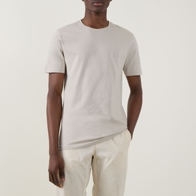 Model wearing Hugo Boss Orange Tales Logo T-Shirt in beige, crew neck with chest logo patch, paired with cream trousers.