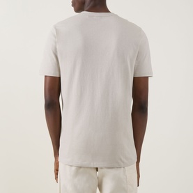 Model wearing Hugo Boss Orange Tales Logo T-Shirt in beige. Rear view showing short sleeves, round neck, and straight hemline. Styled with cream
