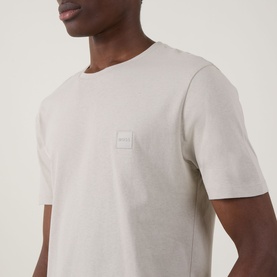 Model wearing Hugo Boss Orange Tales Logo T-Shirt in beige, featuring a small logo patch on the chest, crew neck, and short sleeves.