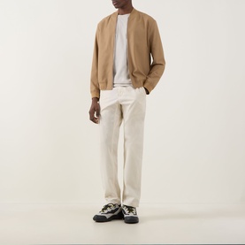 Model wearing Hugo Boss Orange Tales Logo T-Shirt in beige, styled with a camel bomber jacket, cream trousers, and chunky trainers.