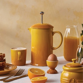 Le Creuset Stoneware Cafetiere With Metal Press 1L in yellow, styled with matching egg cup, mug and jar in honey-toned breakfast setting