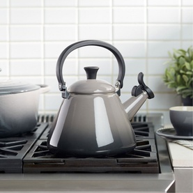 Le Creuset Kone Kettle With Fixed Whistle 1.6L in grey, enamel finish with fixed handle, styled on a gas hob with matching cookware