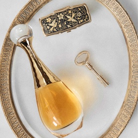 Dior J'adore L'Or Parfum in gold bottle displayed on ornate gold-rimmed plate with decorative compact and key
