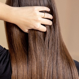 Sisley Revitalising Nourishing Shampoo lifestyle shot showing smooth, glossy, straight brunette hair with a hand running through it