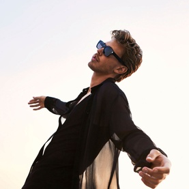 Model wearing black open shirt and sunglasses, arms outstretched, evoking the free spirit of YVES SAINT LAURENT MYSLF Eau de Parfum 60ml