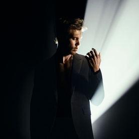 Model with Yves Saint Laurent MYSLF Eau de Parfum 60ml, black lacquer bottle with YSL Cassandre logo, wearing dark blazer in dramatic lighting