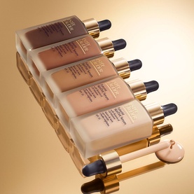 Est&eacute;e Lauder Futurist SkinTint Serum Foundation SPF 20 in five shades, 30ml dropper bottles with gold caps on golden background
