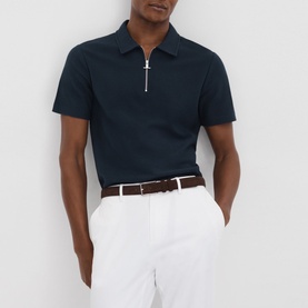 Model wearing Reiss Felix Half-Zip Polo Shirt in blue, textured cotton with silver-tone half-zip, styled with white shorts and brown belt