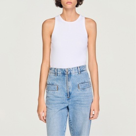 Model wearing Sandro Logo Tank Top in white ribbed cotton, round neck, sleeveless, paired with light blue high-waist jeans