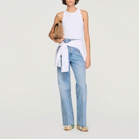 Model wearing Sandro Logo Tank Top in white, tied at waist, styled with light blue straight-leg jeans and gold sandals, carrying a tan bag
