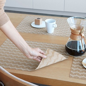 Chilewich Swing Rectangle Placemat in yellow, shown on wooden table with coffee set, hand folding corner to reveal reversible pattern