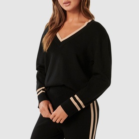 Model wearing Forever New Hattie Knit Sweater in black with gold contrast V-neckline and striped ribbed cuffs, styled with matching trousers