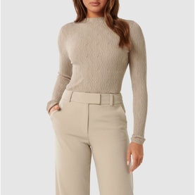 Model wearing Forever New Everley Wave Top in beige with mock neckline, long sleeves and wave pattern, styled with tailored trousers