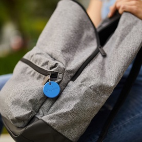 Chipolo ONE Bluetooth Item Finder in blue, disc style tracker attached to zip of grey fabric bag
