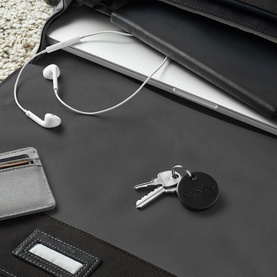 Chipolo ONE Bluetooth Item Finder in black, disc style tracker on a keyring, styled with wired earphones and a laptop bag