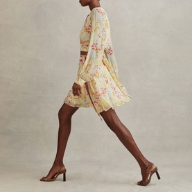 Model wearing Reiss Lyla Floral Print Mini Skirt in pink with tie waist, styled with a matching top and brown heeled mules