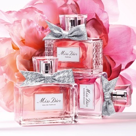 Dior Miss Dior Parfum collection of three pink glass bottles with grey houndstooth bows, displayed among pink peony blooms