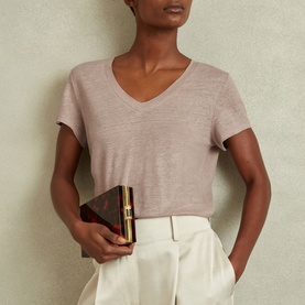 Model wearing Reiss Lottie Marled Solid T-Shirt in pink linen, V-neckline, short sleeves, styled with white wide-leg trousers and dark clutch bag
