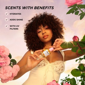 Model with GISOU Honey Infused Hair Perfume Floral Edition Wild Rose 15ml, holding bottle, surrounded by pink roses, pastel sky background
