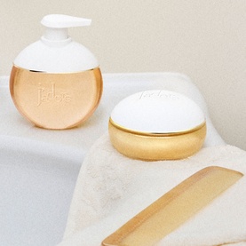 Dior J'adore Les Adorables Shower Gel in gold and white pump bottle, styled alongside a matching lidded pot on marble surface.