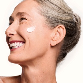 Model with Shiseido Concentrated Supreme Cream applied to cheek, smiling, showing moisturiser texture on skin