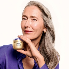 Model with Shiseido Concentrated Supreme Cream Jar & Refill Duo, holding gold-lidded cream jar, wearing purple satin shirt