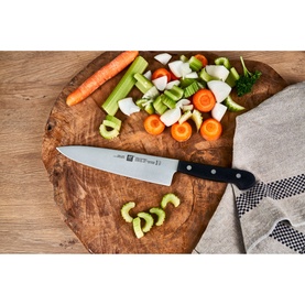 Zwilling Gourmet Chef's Knife on a rustic wooden board with chopped vegetables including carrots, celery and radish