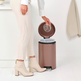 Brabantia NewIcon Pedal Bin 12L in taupe, lid open, styled in a bathroom setting with model's hand placing item inside