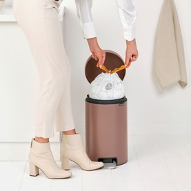 Model with Brabantia NewIcon Pedal Bin 12L in taupe, lid open as liner bag is inserted, styled with neutral tones throughout