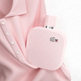 LACOSTE L12.12 Rose Eau de Parfum 100ml, square blush-pink textured bottle with silver crocodile logo, styled with pink fabric backdrop